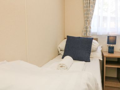A bedroom with a single bed with white sheets and a dark blue pillow next to a wooden nightstand with a black lamp at 23 Manleigh Park Combe Martin