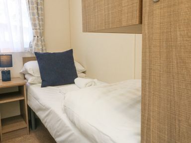 A single bed with white bedding and a dark blue pillow next to a wooden bedside table with a lamp at 23 Manleigh Park in Combe Martin