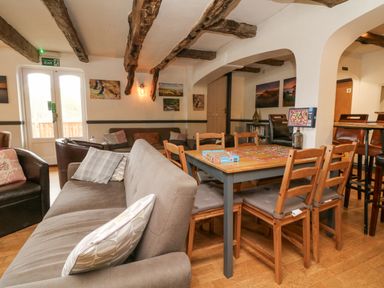 A living area with a gray sofa throw pillows wooden table and chairs exposed ceiling beams and several framed pictures on walls at 23 Manleigh Park in Combe Martin