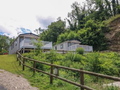 Two small houses with white railings on a grassy hillside with a wooden fence and trees at 23 Manleigh Park in Combe Martin