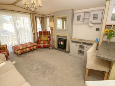 A living room with plaid armchairs and ottoman a fireplace and a wall cabinet at The Boathouse in East Wittering