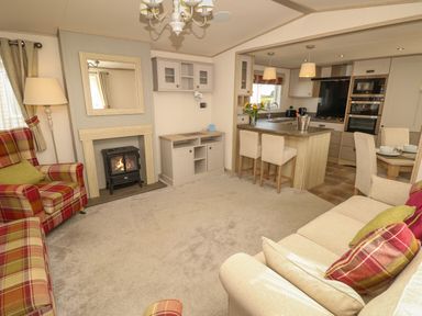 A living room with a fireplace armchairs sofas and a kitchen island with bar stools at The Boathouse in East Wittering