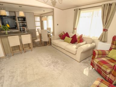 A living room with beige sofa and armchairs next to a dining area and kitchen at The Boathouse in East Wittering