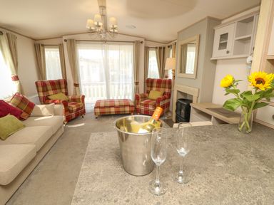 A living room with two plaid armchairs a sofa and a bouquet of sunflowers on the counter at The Boathouse in East Wittering