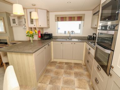 A kitchen with gray countertops built in oven microwave sink window and flowers on the counter at The Boathouse in East Wittering