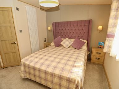 A bedroom with a bed with plaid bedding and cushions bedside tables and wall lights at The Boathouse in East Wittering