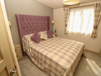A bedroom with a double bed plaid bedspread and curtains and a purple padded headboard at The Boathouse in East Wittering