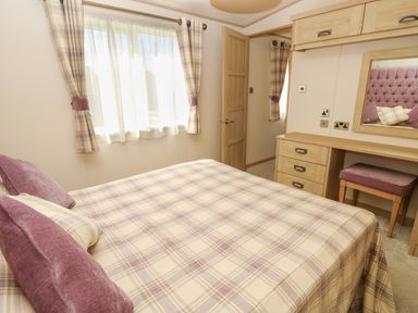 A bedroom with a double bed, a dressing table with mirror and stool, plaid curtains, and a wooden door at The Boathouse in East Wittering