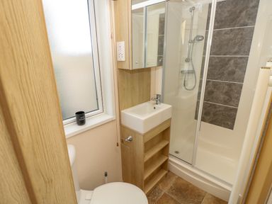 A bathroom with a toilet a small sink a cabinet a shower with sliding doors and a frosted window at The Boathouse in East Wittering