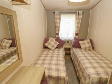 A bedroom with two single beds a window with curtains and a wooden nightstand between the beds at The Boathouse in East Wittering