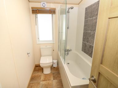 A bathroom with a toilet beside a window and a bathtub with a shower at The Boathouse in East Wittering