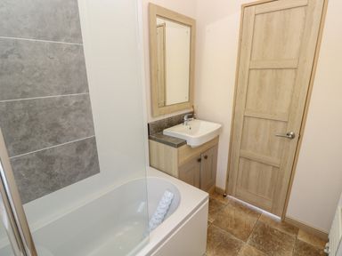 A bathroom with a bathtub sink mirror wooden door and tiled floor at The Boathouse in East Wittering