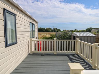An outdoor deck with railings attached to a beige siding building overlooking a field and a small shed at The Boathouse in East Wittering