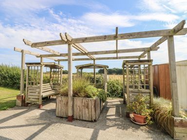 A wooden pergola structure with built-in benches and planters in a garden area at The Boathouse in East Wittering