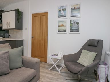 A living room with a gray armchair and sofa with pillows wooden door and framed pictures on the wall at Don's Lodge Grasmere 3 White Cross Bay near Windermere