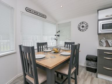 Dining area with a wooden table set for four black chairs a wall clock and kitchen cabinets at Don's Lodge in Grasmere 3 White Cross Bay near Windermere