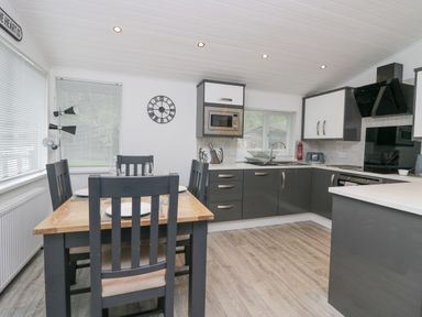 A kitchen with dark cabinets and a wooden dining table with four chairs at Don's Lodge in Grasmere 3 White Cross Bay near Windermere