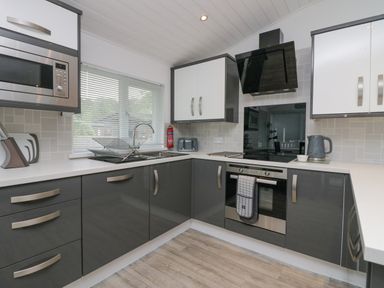 A kitchen with gray and white cabinets a microwave oven a stovetop with an oven a dish drying rack on the counter and a kettle at Don's Lodge in Grasmere 3 White Cross Bay near Windermere