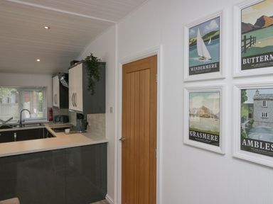 A kitchen with gray cabinets a white countertop a wooden door and four framed pictures on a wall at Don's Lodge in Grasmere 3 White Cross Bay near Windermere