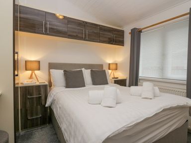 A bedroom with a double bed with pillows and rolled towels bedside tables with lamps and overhead cabinets at Don's Lodge Grasmere 3 White Cross Bay near Windermere