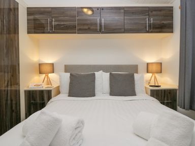 A bedroom with a bed with white linens and gray pillows and lamps on side tables at Don's Lodge in Grasmere 3 White Cross Bay near Windermere