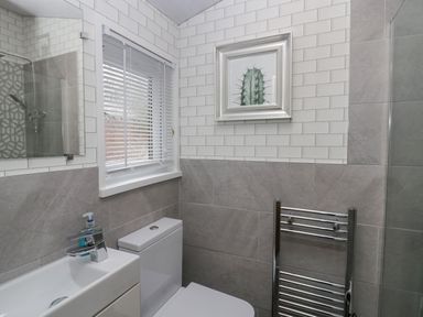 A bathroom with a toilet sink and a towel rack a window with blinds and a framed cactus picture on the wall at Don's Lodge in Grasmere 3 White Cross Bay near Windermere