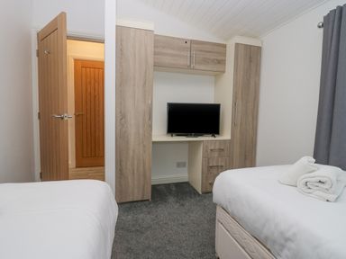 A bedroom with two beds a television on a wooden cabinet and an open door at Don's Lodge in Grasmere 3 White Cross Bay near Windermere