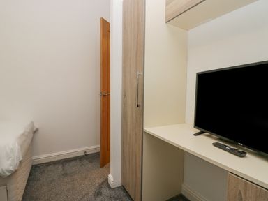 A bedroom corner with a bed, an open wooden door, a wardrobe, and a desk with a television and remote at Don's Lodge in Grasmere 3 White Cross Bay near Windermere