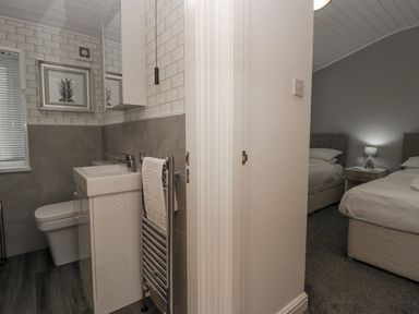 A bathroom with a sink, toilet, towel rack, and framed picture beside a bedroom with two beds, nightstand, and lamp at Don's Lodge in Grasmere 3 White Cross Bay near Windermere