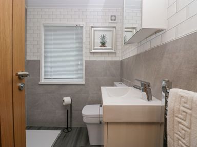 A bathroom with a sink, toilet, towel on a rail, framed pineapple picture and window blinds at Don's Lodge in Grasmere 3 White Cross Bay near Windermere