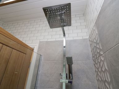 A shower area with a square rainfall showerhead and a handheld showerhead mounted on a tiled wall at Don's Lodge Grasmere 3 White Cross Bay near Windermere