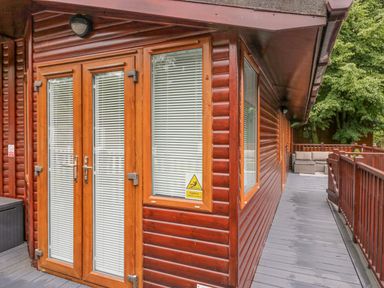 Wooden lodge exterior with glass door and windows and a deck with railing and outdoor seating at Don's Lodge Grasmere 3 White Cross Bay near Windermere