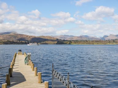 A wooden dock extending into a lake with mountains and a boat in the background at Don's Lodge in Grasmere 3 White Cross Bay near Windermere