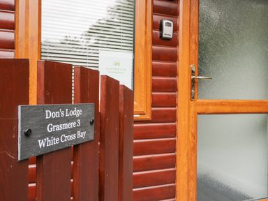 A wooden door and window next to a wooden fence with a sign reading Dons Lodge Grasmere 3 White Cross Bay near Windermere