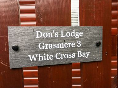 A sign on a wooden fence that reads Dons Lodge Grasmere 3 White Cross Bay