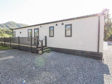 An exterior view of a single-story building with a gravel foreground and a wooden deck railing at Saorsa in St Fillans
