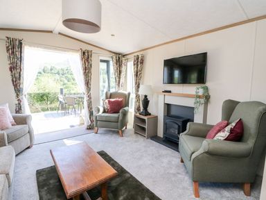 A living room with armchairs a coffee table a TV above a fireplace and glass doors opening to an outdoor patio at Saorsa in St Fillans