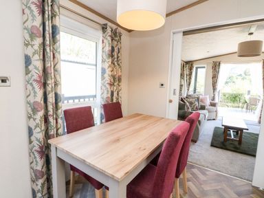 A dining area with a wooden table and four red chairs next to patterned curtains and a window at Saorsa in St Fillans