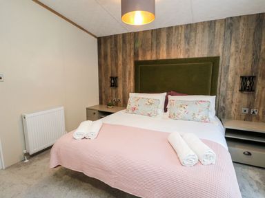 A bedroom with a double bed with floral cushions and pink blanket at Saorsa in St Fillans