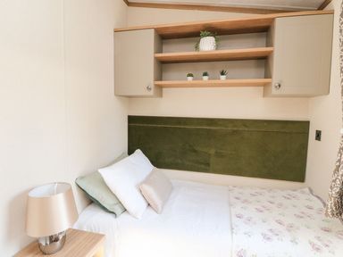 A bedroom with a single bed beside a wooden nightstand with a lamp and wall shelves with small plants at Saorsa in St Fillans