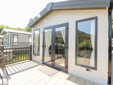 A deck outside a small building with glass doors and windows reflecting trees and hills at Saorsa in St Fillans