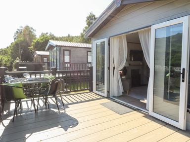 An outdoor deck with a round table and chairs next to an open glass door leading to a living room at Saorsa in St Fillans