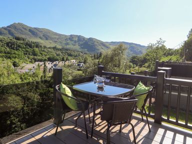 A balcony with a glass table and four chairs overlooking mountains and houses at Saorsa in St Fillans