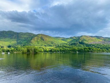 A body of water with trees and hills in the background at Saorsa in St Fillans