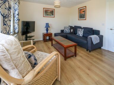 A living room with a dark blue sofa wooden coffee table wooden side table with blue lamp armchair with cushions and a television at 74 Reap Lane Southwell near Weston