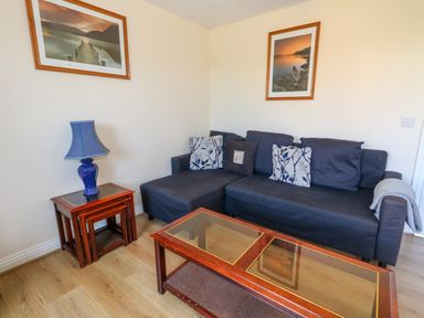 A living room with a dark sofa cushions tables a blue lamp and framed pictures on the wall at 74 Reap Lane Southwell near Weston