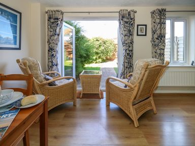 A sitting area with two wicker chairs and a small table by an open glass door leading to a garden at 74 Reap Lane Southwell near Weston