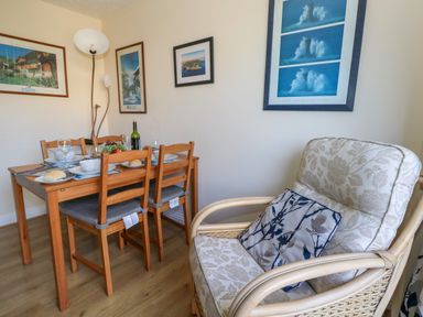 A dining table with four wooden chairs set with plates glasses and fruit next to a cushioned armchair with a pillow at 74 Reap Lane Southwell near Weston