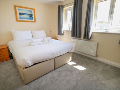 A bedroom with a double bed with white linens two windows with gray curtains and wooden bedside tables at 74 Reap Lane Southwell near Weston