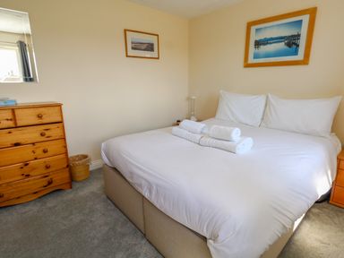 A bedroom with a double bed and rolled towels on it a wooden chest of drawers and framed pictures on the walls at 74 Reap Lane in Southwell near Weston